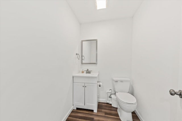 half bath featuring vanity, toilet, wood finished floors, and baseboards