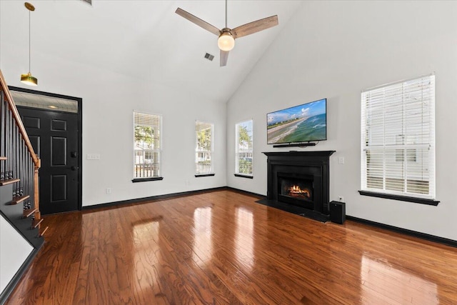 unfurnished living room featuring baseboards, stairway, a fireplace with flush hearth, wood finished floors, and high vaulted ceiling