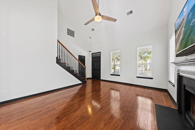 unfurnished living room featuring visible vents, stairs, a fireplace with flush hearth, and wood finished floors