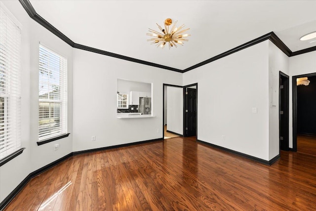 spare room with an inviting chandelier, wood finished floors, baseboards, and ornamental molding