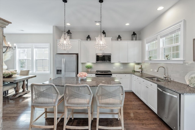 kitchen featuring a sink, white cabinets, appliances with stainless steel finishes, a center island, and dark stone counters