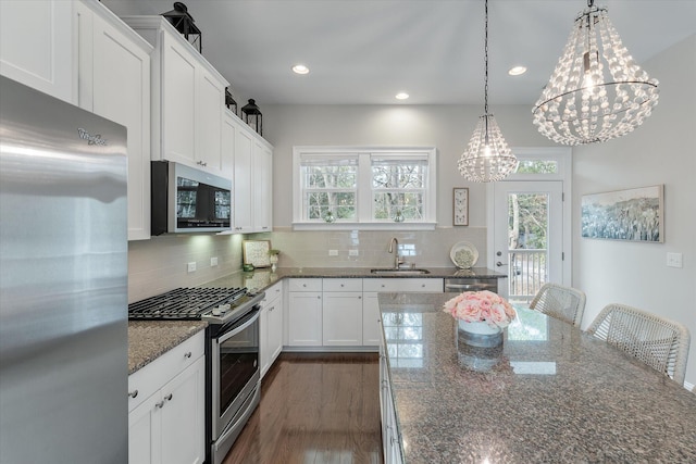 kitchen with white cabinets, appliances with stainless steel finishes, dark stone countertops, pendant lighting, and a sink