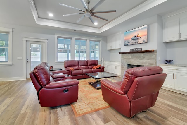 living room with ornamental molding, a tray ceiling, a fireplace, light wood finished floors, and ceiling fan