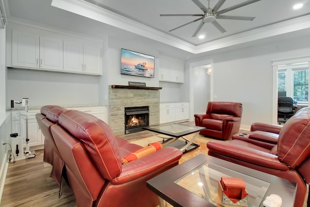 living area featuring crown molding, a stone fireplace, recessed lighting, light wood-style floors, and a ceiling fan