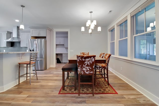 dining space with light wood finished floors, a notable chandelier, baseboards, and visible vents