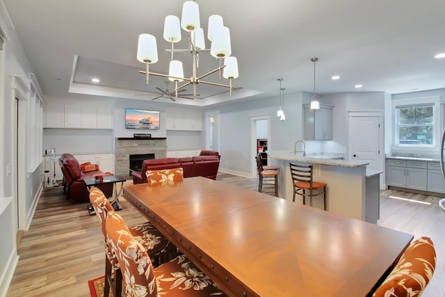 dining room with recessed lighting, a raised ceiling, light wood-style flooring, and a fireplace