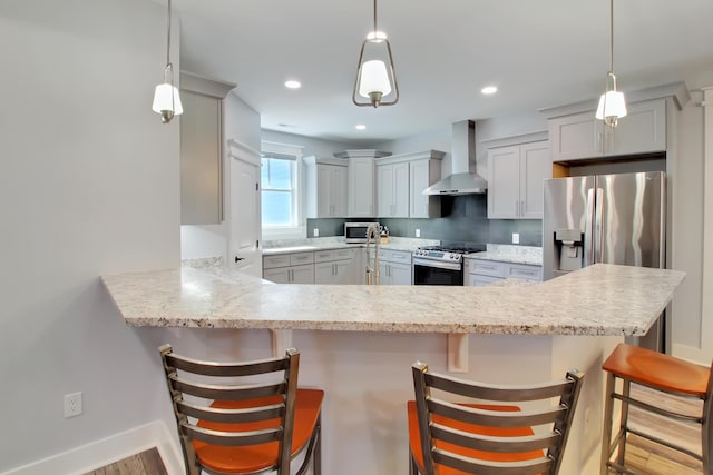 kitchen with baseboards, a peninsula, recessed lighting, stainless steel appliances, and wall chimney range hood