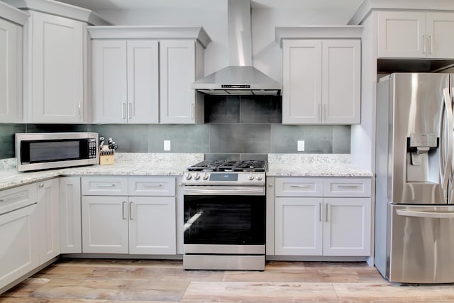 kitchen featuring tasteful backsplash, light wood-type flooring, light stone counters, stainless steel appliances, and wall chimney exhaust hood