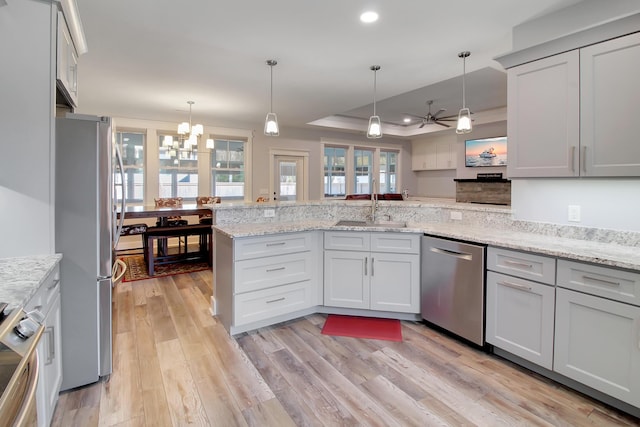 kitchen with a tray ceiling, light wood-style flooring, a peninsula, a sink, and appliances with stainless steel finishes