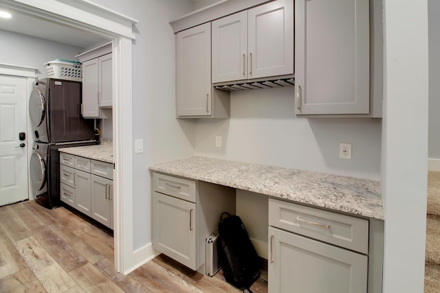 kitchen with stacked washer / drying machine, light stone countertops, built in study area, and light wood finished floors