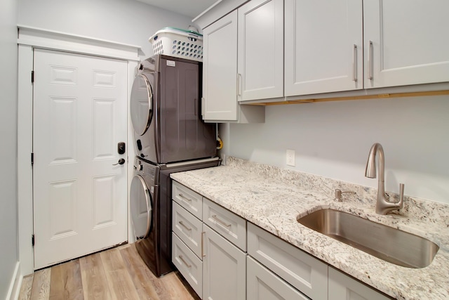 laundry room with cabinet space, stacked washer and clothes dryer, light wood-type flooring, and a sink