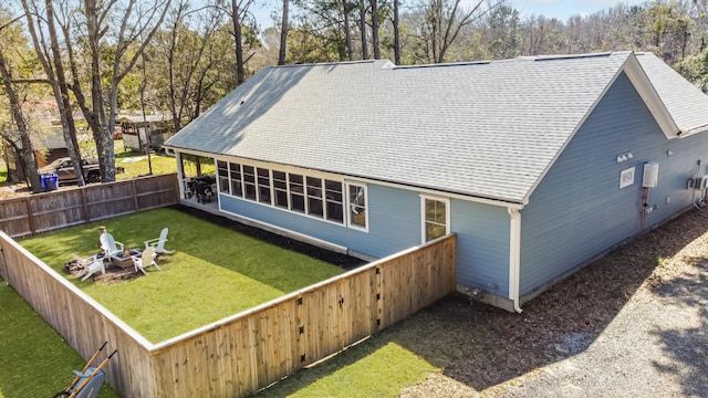 back of house featuring a fenced backyard, a fire pit, a shingled roof, and a lawn