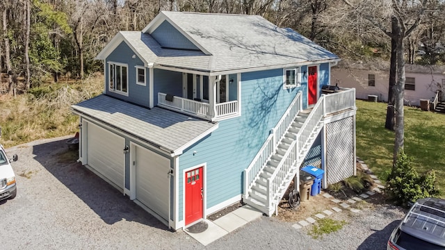 view of front of home with a shingled roof, stairway, a front yard, covered porch, and an attached garage