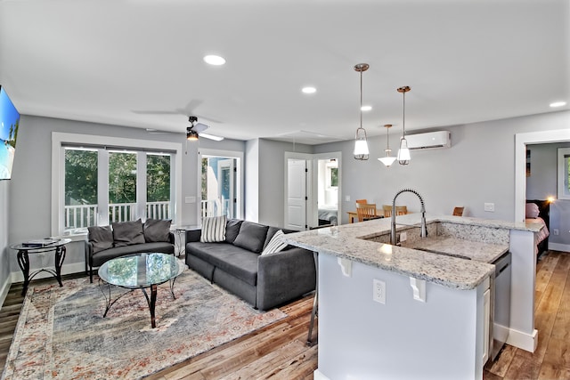 kitchen featuring open floor plan, a center island with sink, dishwasher, light stone counters, and hardwood / wood-style flooring