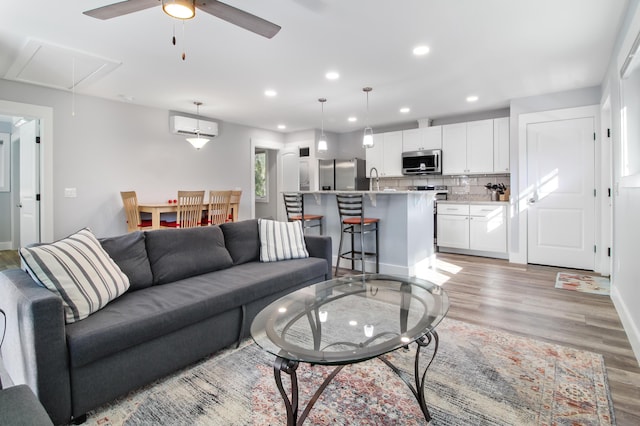 living room with ceiling fan, attic access, recessed lighting, light wood-style flooring, and a wall mounted AC