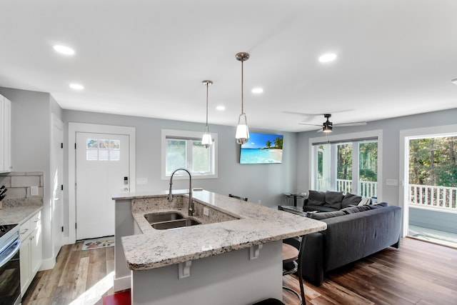 kitchen with a kitchen island with sink, a sink, wood finished floors, recessed lighting, and white cabinets