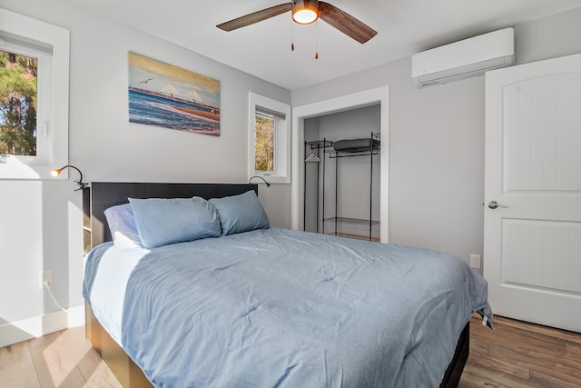 bedroom with a ceiling fan, a wall unit AC, and wood finished floors