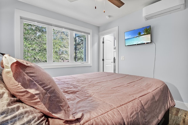 bedroom with a wall unit AC, wood finished floors, and ceiling fan