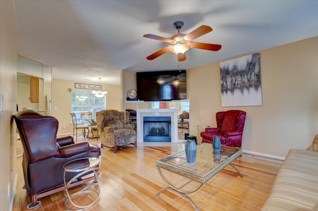 living room featuring wood-type flooring, ceiling fan with notable chandelier, and a textured ceiling