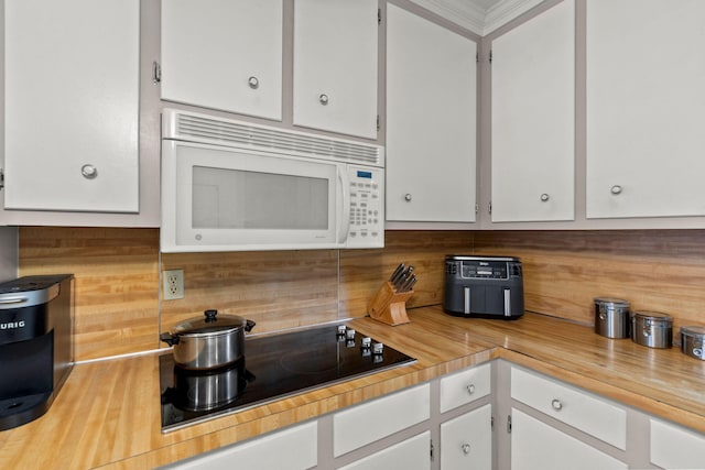 kitchen with backsplash, black electric stovetop, and white cabinets