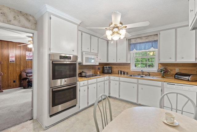 kitchen featuring white cabinetry, sink, wooden walls, white appliances, and light carpet