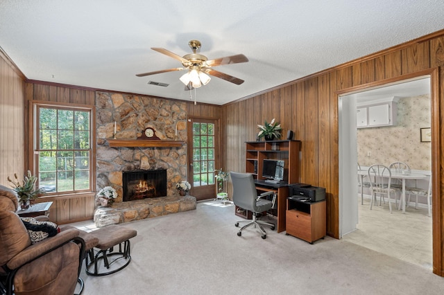 office space featuring ceiling fan, a stone fireplace, wood walls, crown molding, and light colored carpet