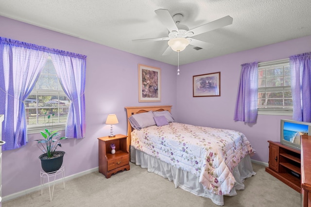 bedroom with multiple windows, a textured ceiling, light colored carpet, and ceiling fan