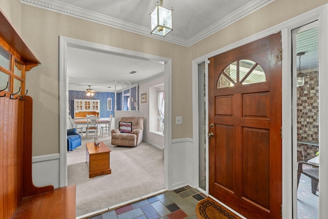 foyer with dark colored carpet, ceiling fan, crown molding, and a textured ceiling