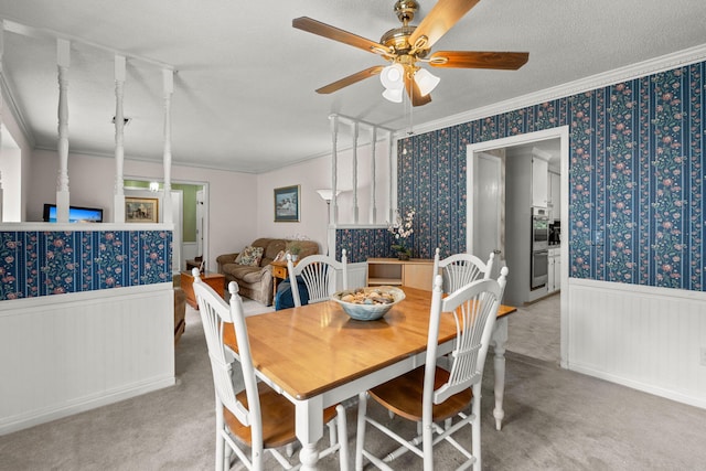 dining area featuring wood walls, ceiling fan, ornamental molding, a textured ceiling, and light colored carpet