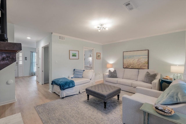 living room with ornamental molding, light wood-style flooring, visible vents, and baseboards