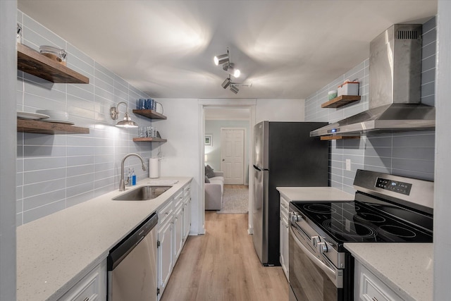 kitchen with tasteful backsplash, wall chimney exhaust hood, stainless steel appliances, open shelves, and a sink