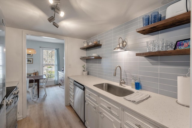 kitchen with open shelves, tasteful backsplash, appliances with stainless steel finishes, a sink, and light wood-type flooring