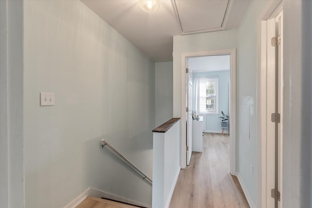 corridor with light wood finished floors, an upstairs landing, and baseboards