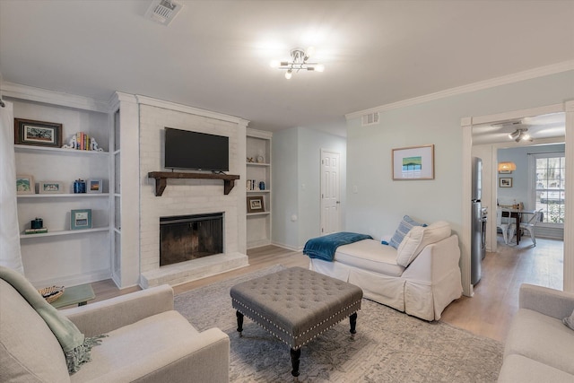 living area with light wood-style floors, a brick fireplace, visible vents, and ornamental molding