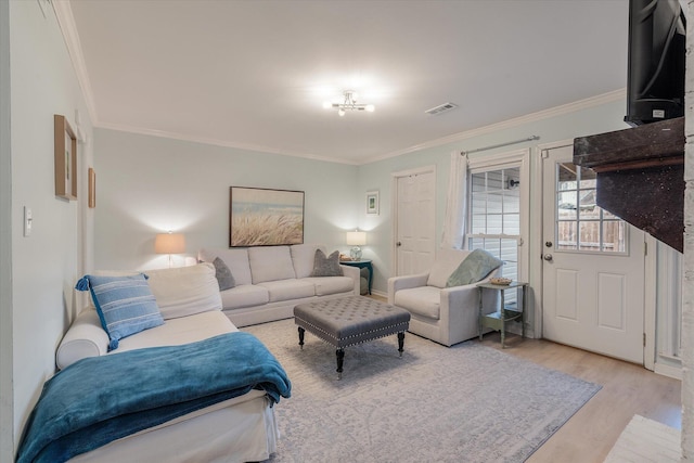 living room with baseboards, light wood-type flooring, visible vents, and crown molding