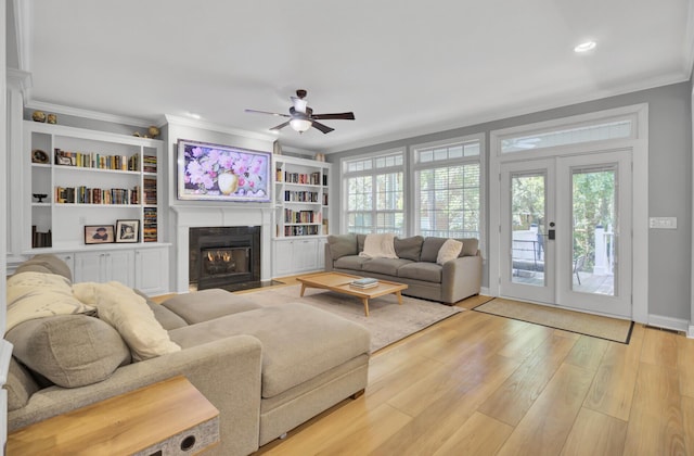 living area with ceiling fan, crown molding, a fireplace with flush hearth, plenty of natural light, and wood finished floors
