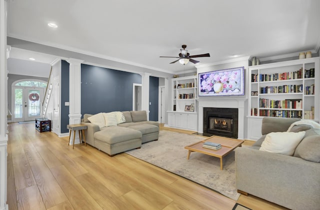 living room featuring decorative columns, crown molding, a ceiling fan, light wood finished floors, and a fireplace with flush hearth