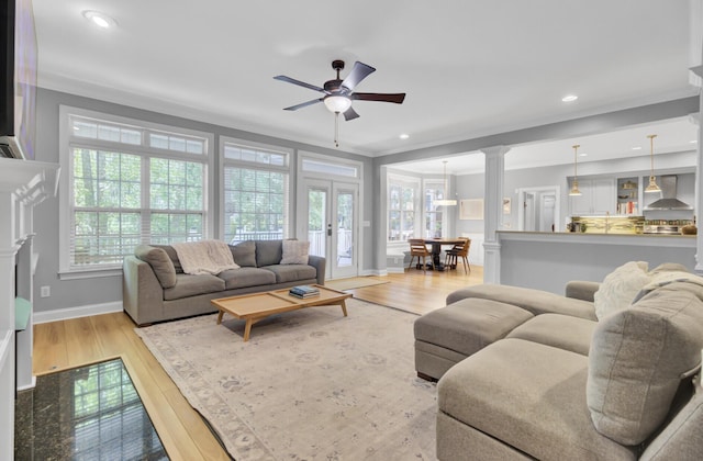 living area featuring ornamental molding, wood finished floors, baseboards, a ceiling fan, and decorative columns