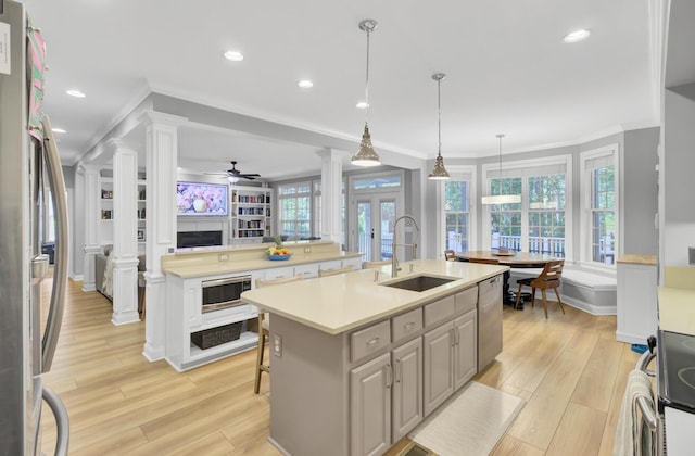 kitchen featuring a sink, decorative columns, stainless steel appliances, ornamental molding, and a center island with sink