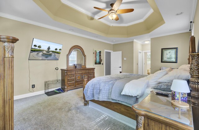 carpeted bedroom with a tray ceiling, ornamental molding, ceiling fan, ensuite bathroom, and baseboards
