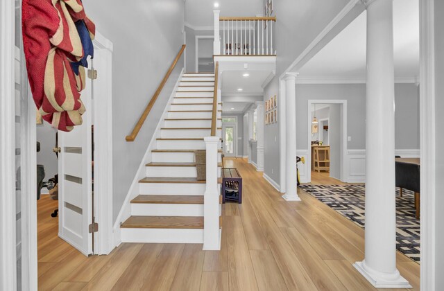 entrance foyer with decorative columns, ornamental molding, wood finished floors, stairs, and baseboards