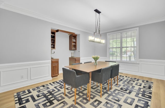 dining space with light wood finished floors, ornamental molding, and wainscoting