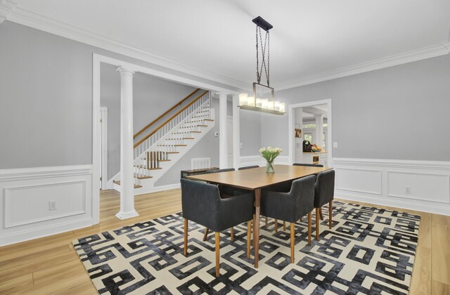 dining space featuring light wood finished floors, stairway, crown molding, ornate columns, and a wainscoted wall