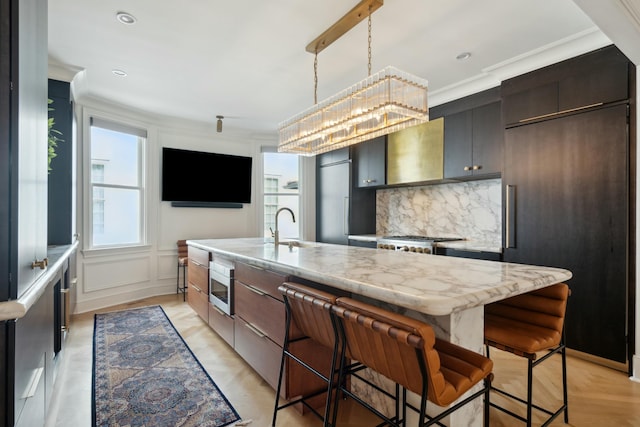 kitchen with stainless steel microwave, a decorative wall, decorative backsplash, a sink, and wall chimney exhaust hood