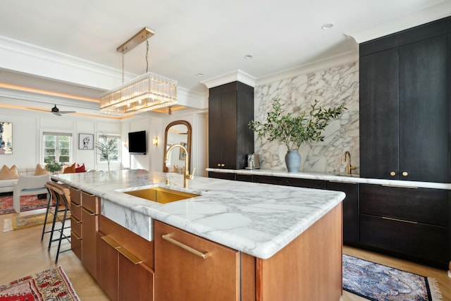 kitchen with light stone counters, a kitchen island with sink, a sink, open floor plan, and crown molding