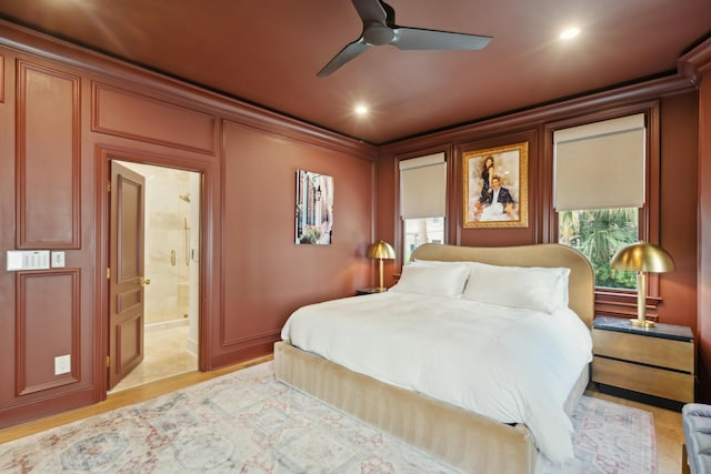 bedroom with a decorative wall, light wood-style flooring, ensuite bathroom, ornamental molding, and ceiling fan