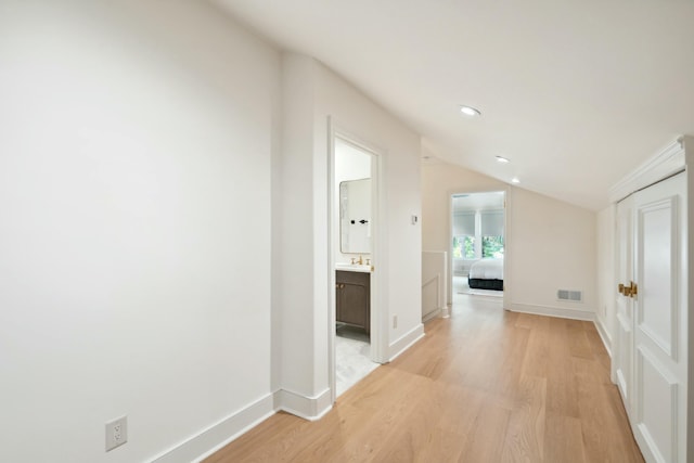 hall featuring vaulted ceiling, light wood-type flooring, visible vents, and baseboards