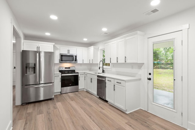 kitchen with sink, light wood-type flooring, white cabinets, and appliances with stainless steel finishes