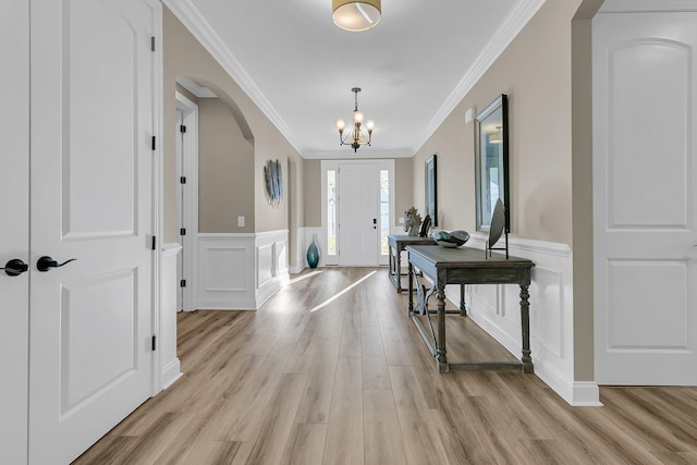 entryway with a wainscoted wall, a notable chandelier, crown molding, light wood-style floors, and arched walkways