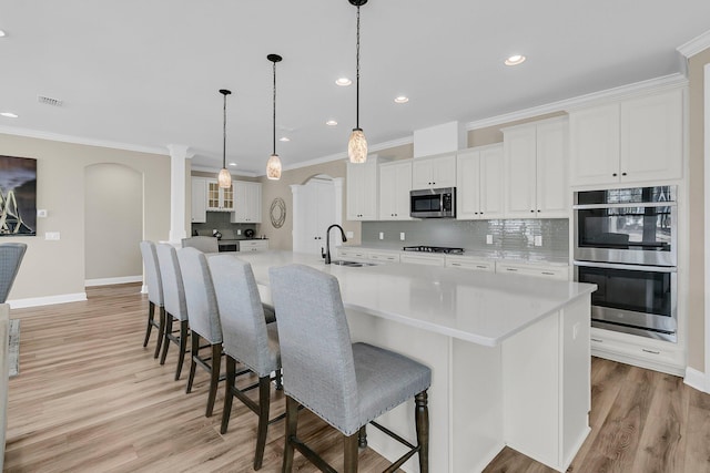 kitchen featuring a sink, white cabinetry, tasteful backsplash, stainless steel appliances, and ornamental molding